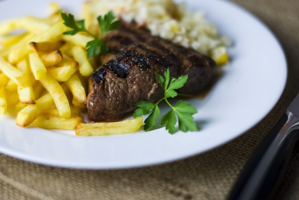 Imagem mostra porção de fritas com carne bem passada e arroz branco.